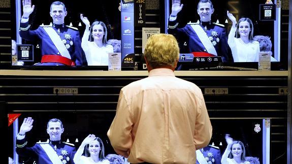Un hombre observa en varias televisiones el saludo de los nuevos Reyes. 