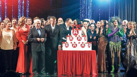 Invitados a la gala y responsables del teatro celebran el cumpleaños con una tarta sobre el escenario.