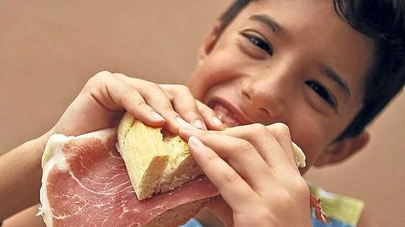 Un niño come un bocadillo de jamón.