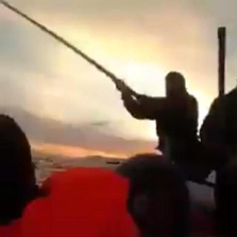 Un guardacostas intenta golpear a los refugiados con un palo.