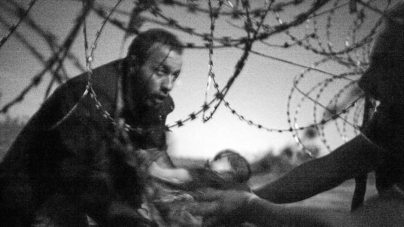 Un hombre entrega un bebé a otro refugiado a través de una alambrada entre Serbia y Hungría. 