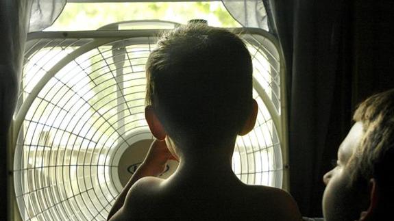 Niños alivian el calor frente a un ventilador en su casa. 