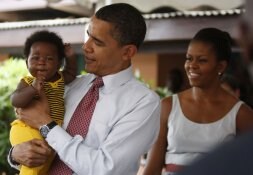 Obama sostiene en brazos a un bebé durante su visita a un hospital de Accra mientras               detrás su esposa, Michelle, esboza una sonrisa. / REUTERS