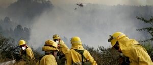 Un grupo de voluntarios colabora en la extinción del fuego en la zona de Tigalate, ayudados desde el aire por un helicóptero./ AFP