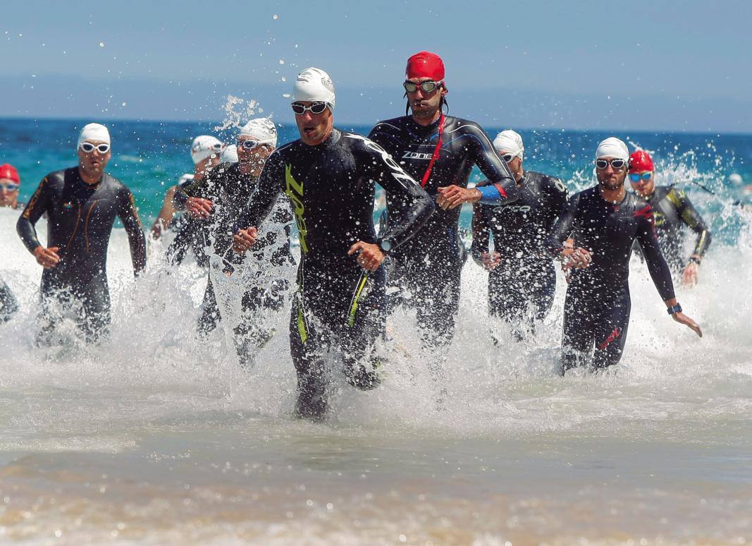 Los participantes en el Medio Ironman de Buelna, saliendo del agua tras finalizar la prueba de natación en la playa de Comillas.
