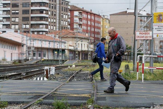 Dos vecinos caminan por el paso a nivel de Pablo Garnica, con la estación de FEVE al fondo