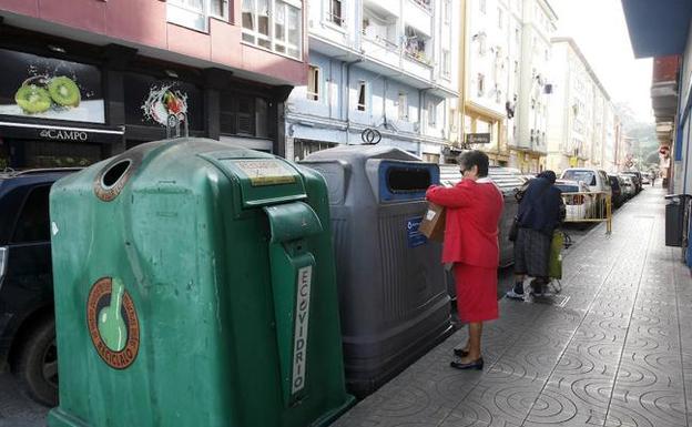 Una mujer deposita cartón en una de las zonas reservadas para los contenedores de basura en La Inmobiliaria