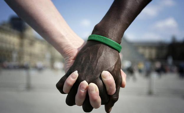 Las manos de una mujer blanca y un hombre negro se entrelazan enfrente del Museo Louvre de Paris.