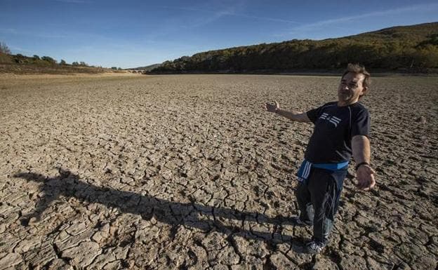 Rafael González camina sobre el suelo agrietado y reseco con el puente de Horna al fondo.