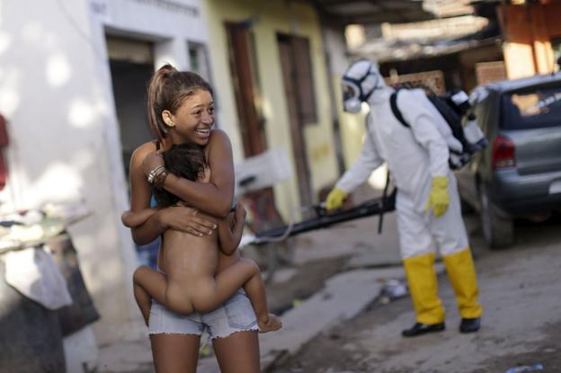 Una mujer brasileña se aleja con su hijo en brazos del operario que rocía insecticida contra el mosquito ‘aedes aegypti’ en una calle de Recife. 