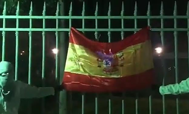 Dos jovenes sujetan la bandera española mientras comienza a arder.