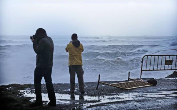 Dos jóvenes sacan fotos de las grandes olas en Comillas durante el último temporal 