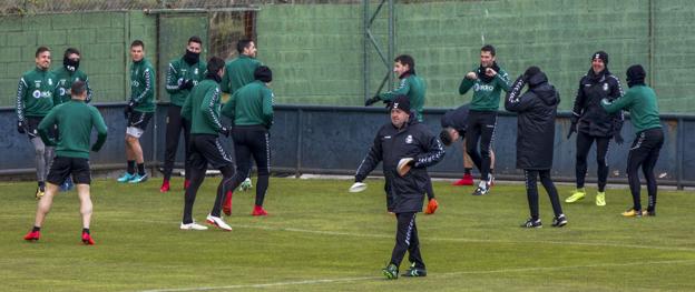 Carlos Pouso coloca unos conos mientras sus futbolistas calientan durante la sesión de entrenamiento de ayer. 