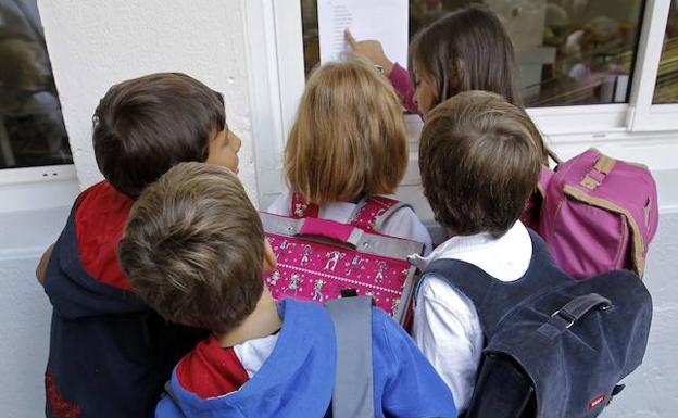 Escolares leen las listas colocadas en el tablón de anuncios del patio de una escuela. 