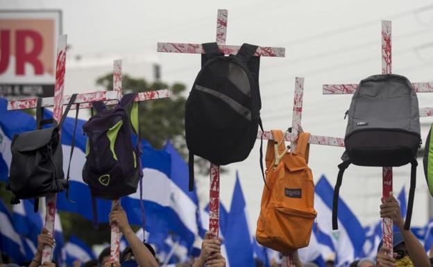 Varios jóvenes sostienen cruces con mochilas en honor a los estudiantes que murieron en manifestaciones en Nicaragua.