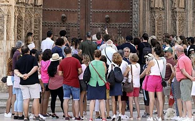 Un gran númeo de turistas contempla la puerta de los Apóstoles en la plaza de la Virgen, en Valencia. 