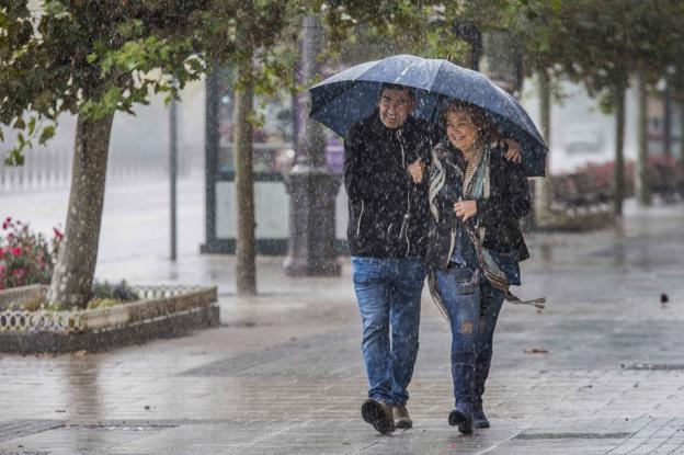 Dos personas se protegen de la lluvia con un paraguas mientras pasean por el centro de Santander. 