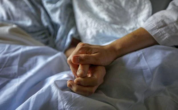 Un familiar coge de la mano a una paciente con cuidados paliativos.
