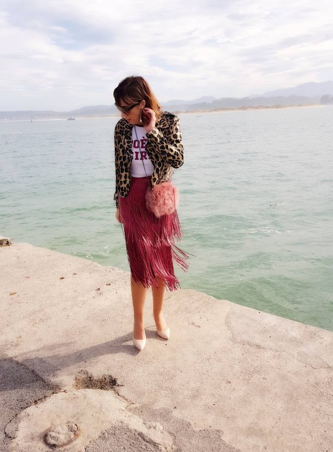 Falda de flecos en un look informal con una camiseta con mensaje y una 'biker' de 'animal print'. Además, le añadimos un bolso de pelo rosa.