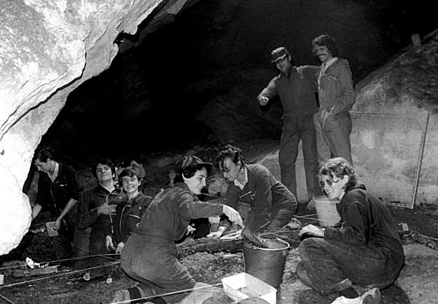  En la cueva. La fotografía, cedida por Lourdes Ortega, esposa de Alfonso Moure, pertenece a la campaña de 1974. Un grupo de alumnos excava en la zona de la antigua boca de la cueva. De pie, Alfonso Moure y Pedro Saura. Entre los alumnos, Carmen Cacho, Federico Bernaldo de Quirós, Isabel Martínez Navarrete, Mercedes Cano y Victoria Cabrera. 