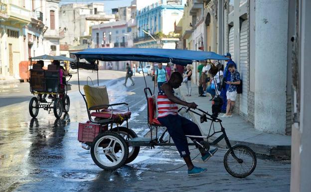 El conductor de un bici-taxi vestido con una camiseta con la bandera estadounidense espera en La Habana.