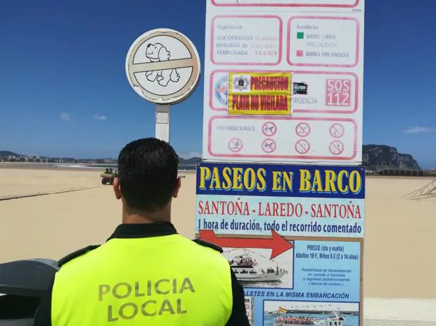 Un policía local de Laredo frente al cartel que informa de que la playa de Laredo no está vigilada. 