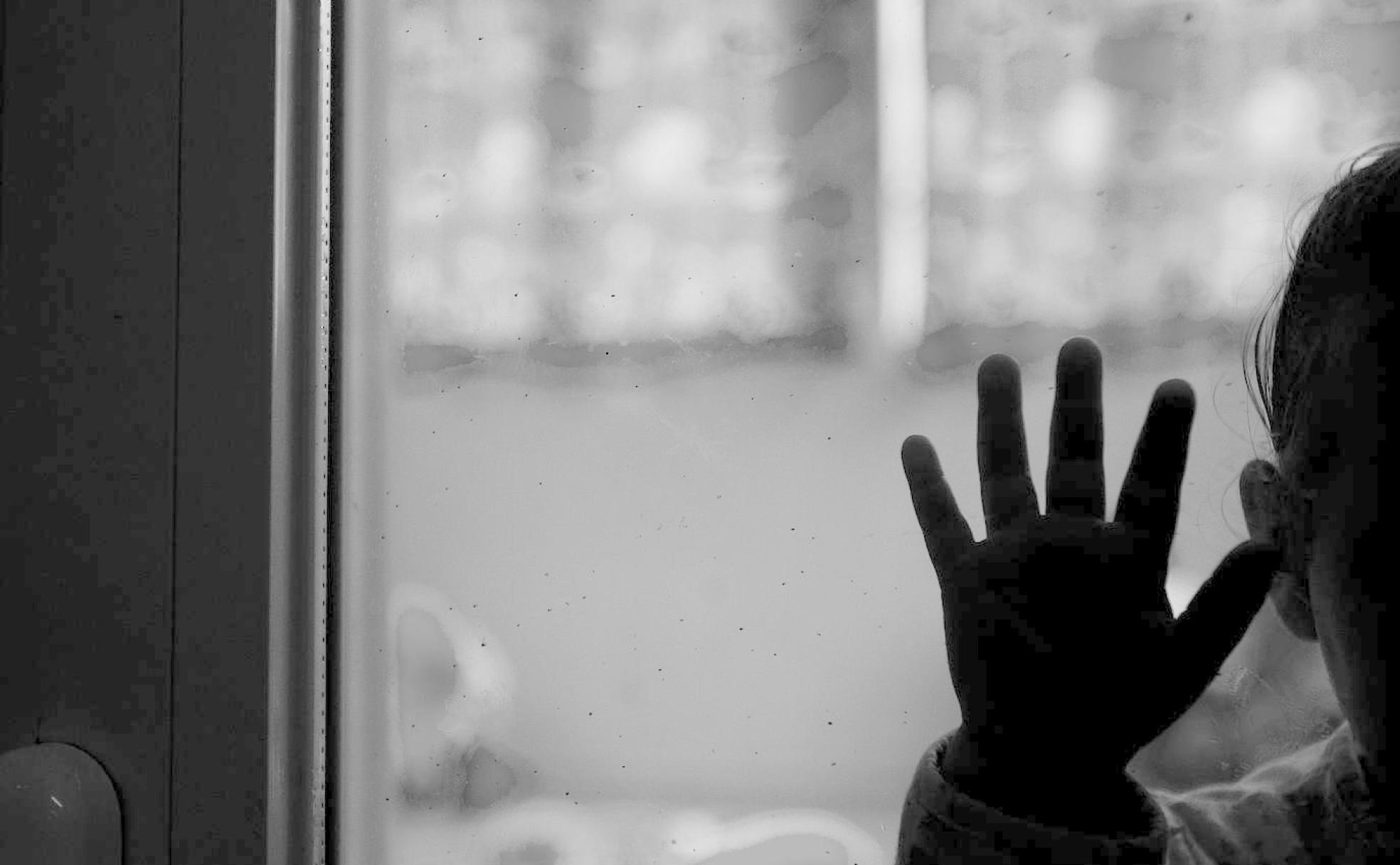 Una niña extiende la mano sobre una ventana. 