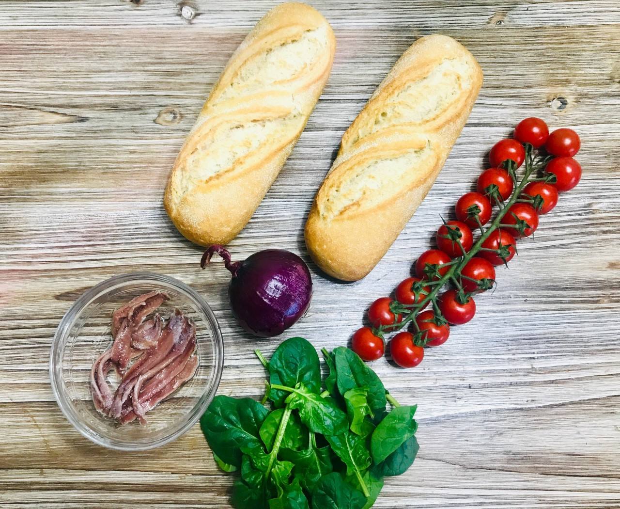 BOCADILLO DE ESPINACAS. Ingredientes: Una lata de anchoas en aceite de oliva, tomatitos cherry, espinacas frescas, cebolla morada, aceite de oliva, crema de vinagre de Módena, sal y semillas de sésamo tostado. Cantidad según comensales.