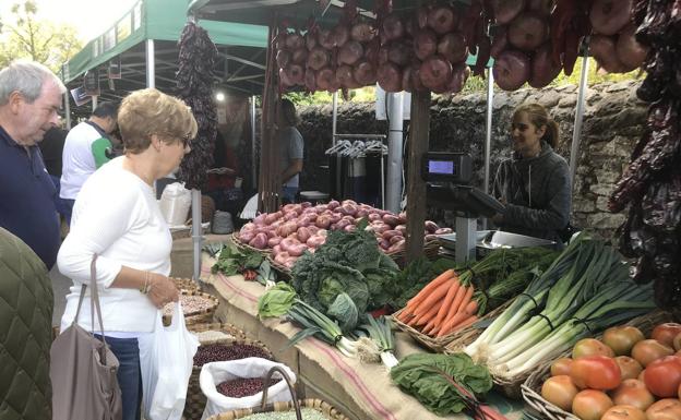 Dos visitantes observan las verduras y las legumbres ofrecidas en uno de los puestos del mercado de Liérganes.