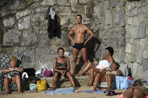 Un grupo de personas toma el sol en 'El Tostadero' en la playa de San Lorenzo de Gijón.