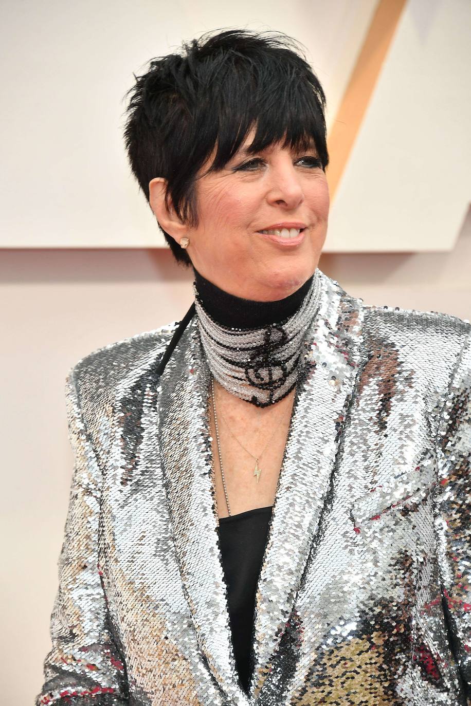 Diane Warren es la compositora de ‘I´m standing with you’, canción que opta al galardón por la ‘Mejor canción’ por la película ‘Un amor inquebrantable’. Para pisar la alfombra roja se ha desmarcado del resto con una americana de ‘paillettes’ metalizadas, un pantalón negro y unos botines negros con tacón de ‘strass’. Además, muy metida en su papel, destaca por una original gargantilla confeccionada con cristales de Swarovski en la que se dibuja una clave de Sol.