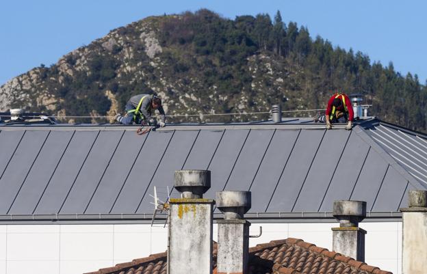 Dos obreros de la empresa que ha puesto el tejado se afanan en reforzar y ajustar las chapas de la cubierta. 