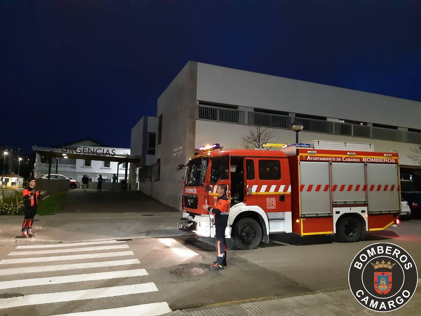 Dos bomberos aplauden junto a la entrada de urgencias del Centro de Salud Camargo Costa de Maliaño.