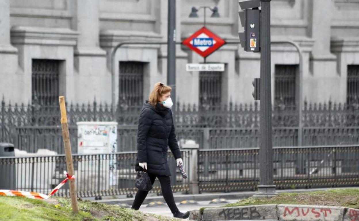 Una mujer con mascarilla pasea junto a la boca del metro de Banco de España, en Madrid