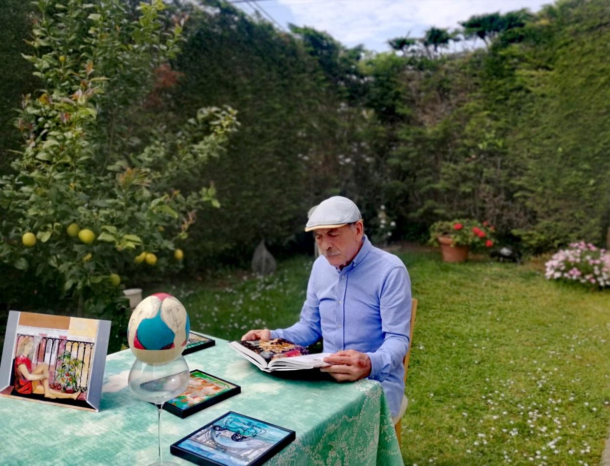 El artista Roberto Orallo lee en el jardín de su casa junto a algunas de sus obras. En primer plano, un cuadro inspirado en el confinamiento. dm