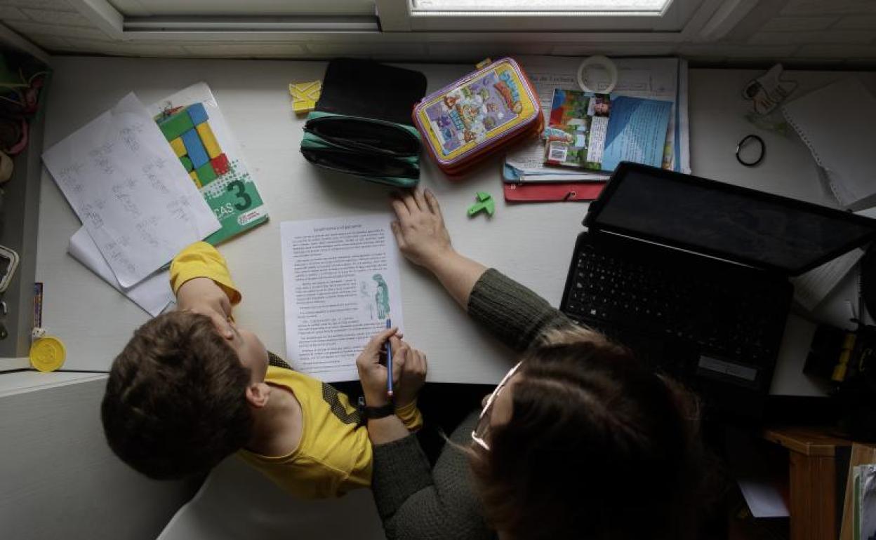 Un niño estudia y hace los deberes en casa con la ayuda de su madre.