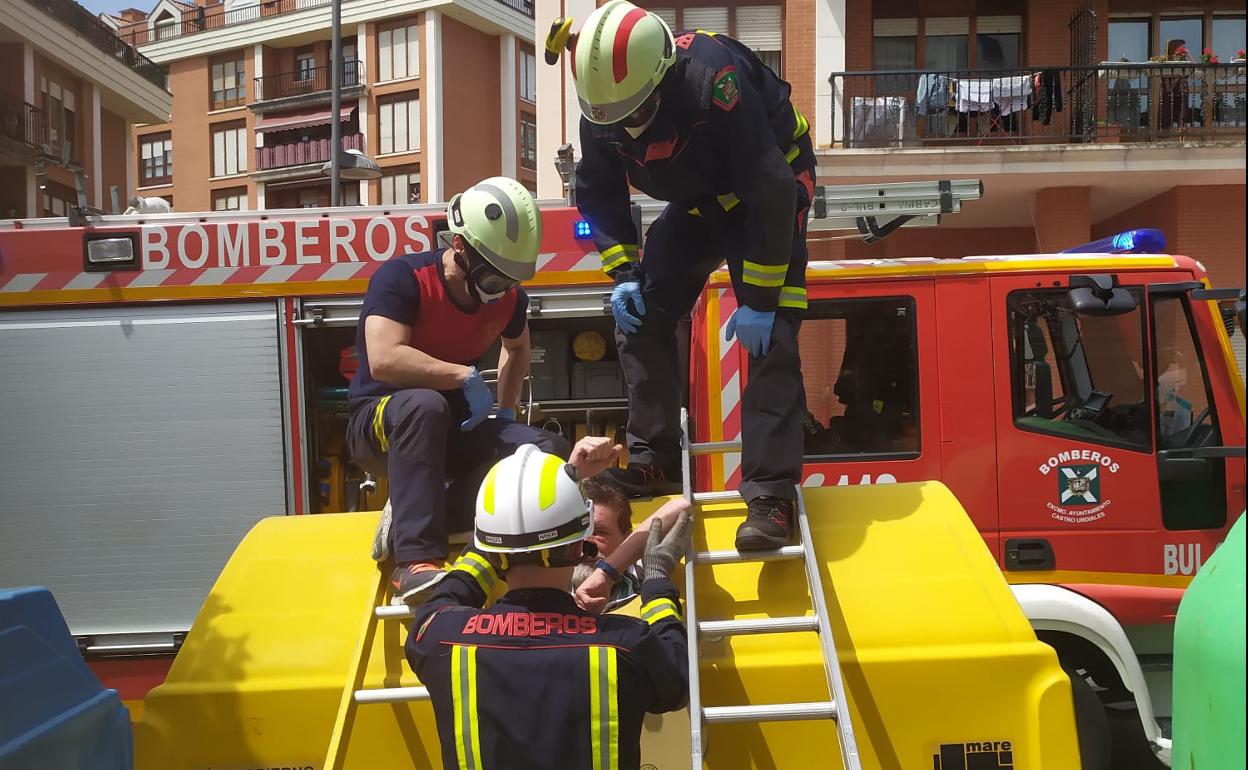 Los bomberos asisten al hombre que está dentro del contenedor amarillo.