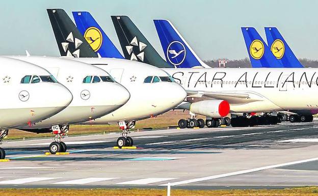 Imagen principal - Aparatos de la flota de Lufthansa aparcados en el aeropuerto de Fráncfort por falta de operaciones. | Área de facturación del aeropuerto de Tokio, que decidió hace tres semanas suspender el 90% de sus vuelos. | Sello que informa de un positivo por coronavirus en un control de pasaportes del espacio Schengen.