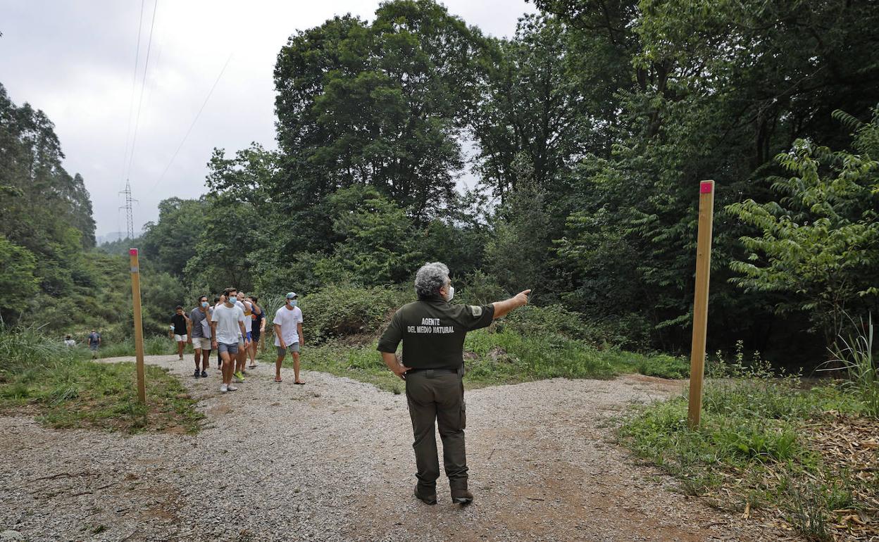 Un agente de Medio Natural muestra el inicio de una ruta a un grupo de caminantes, ya que los indicadores han sido arrancados de los postes