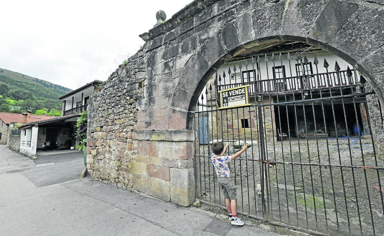 Un niño juega en la verja de la que cuelga un cartel que anuncia la venta de la casa, en la localidad cabezonense de Santibáñez. 