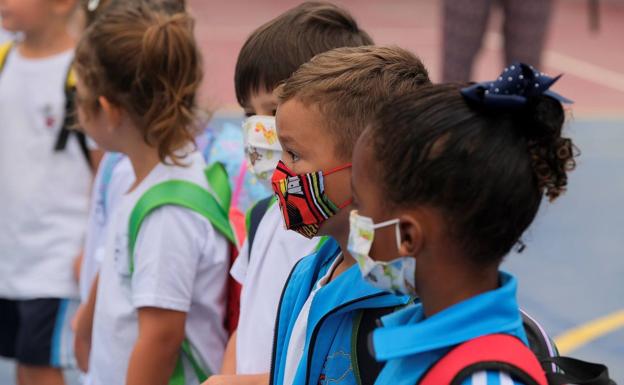 Varios niños con mascarillas, a la entra del colegio. 