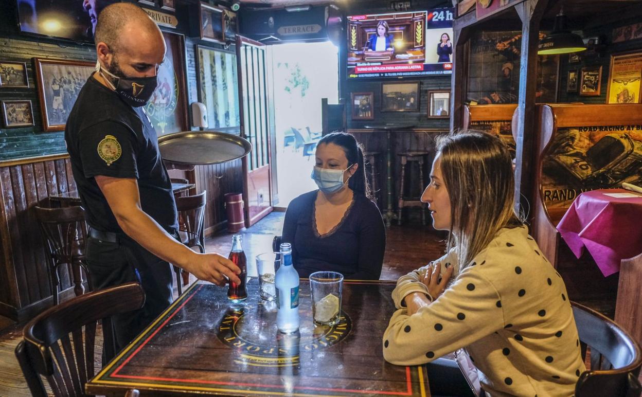 Un camarero de la Taberna Remigio, en La Albericia, sirve a dos clientas dentro del local. 