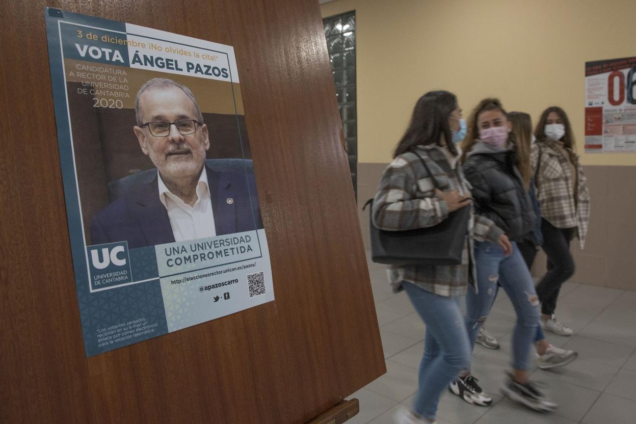 Alumnas del grado en Derecho caminan junto a uno de los carteles electorales del rector y candidato a la reelección, Ángel Pazos, ayer, en la UC. 