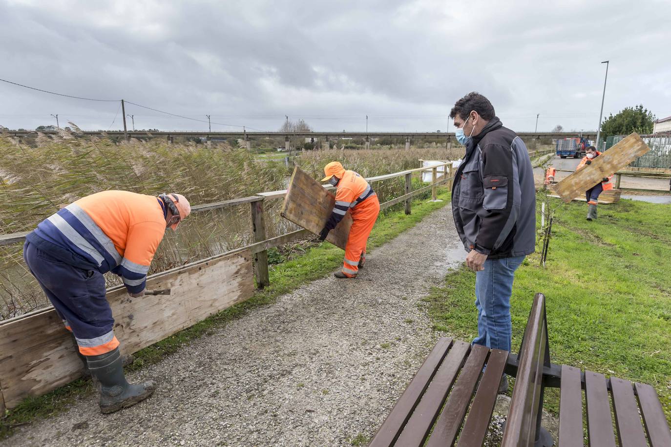 Operarios clavan tablones y extienden una capa de tierra a modo de dique para evitar que el agua vuelva a inundar el barrio de Santiago el Mayor (Nueva Montaña), mientras el vecindario sigue limpiando el barro, colocando sacos a las puertas de sus casas y los bomberos achican el agua acumulada en bajos y garajes.