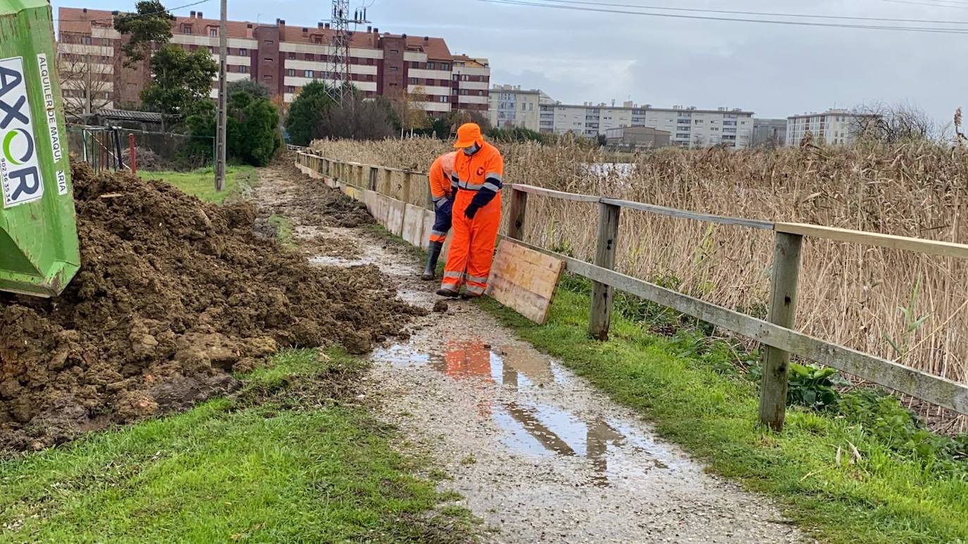 Operarios clavan tablones y extienden una capa de tierra a modo de dique para evitar que el agua vuelva a inundar el barrio de Santiago el Mayor (Nueva Montaña), mientras el vecindario sigue limpiando el barro, colocando sacos a las puertas de sus casas y los bomberos achican el agua acumulada en bajos y garajes.