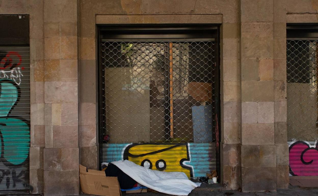 Una persona cubierta con cartones y una manta duerme en plena calle. 