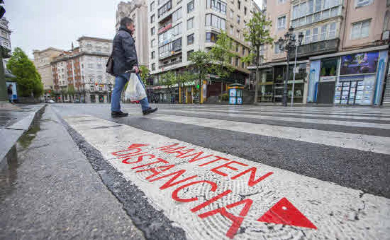 Un peatón cruza por un paso de cebra que recuerda la medida de mantener la distancia durante la crisis sanitaria, en Santander