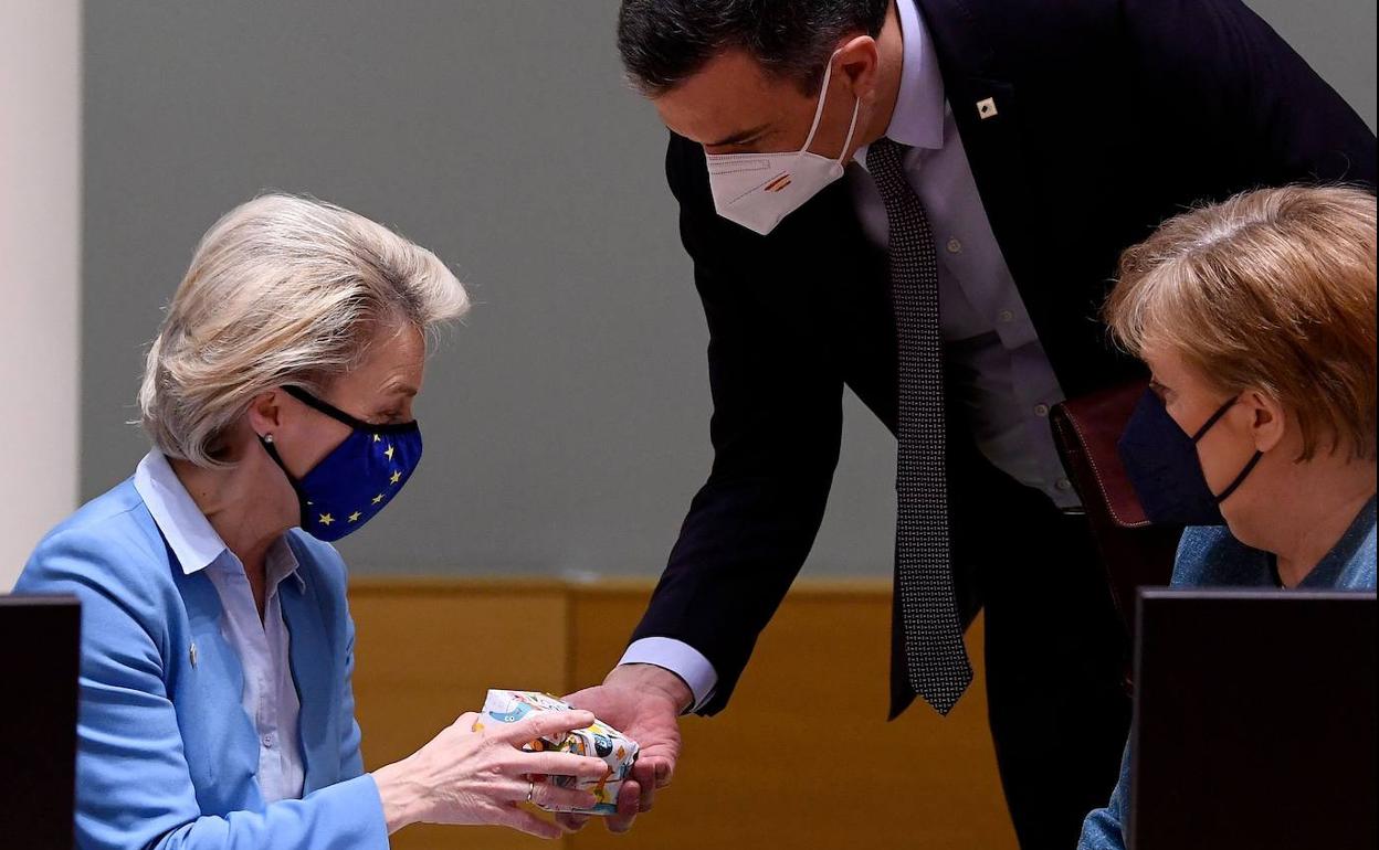 Pedro Sánchez entrega los patucos a Ursula von der Leyen ante la atenta mirada de Angela Merkel.