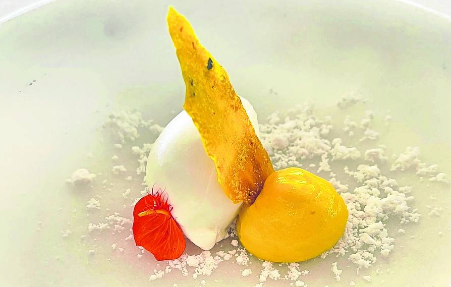 Postre gastronómico. Se llama Lassi y recuerda a una bebida tradicional de la India hecha a base de yogur. Aquí el chef la deconstruye y la transforma en un postre creativo. La base es una tierra de coco a la que se suman la cúrcuma y el mango formando una crema, el azafrán en el crujiente y completa el conjunto un helado de yogur. 