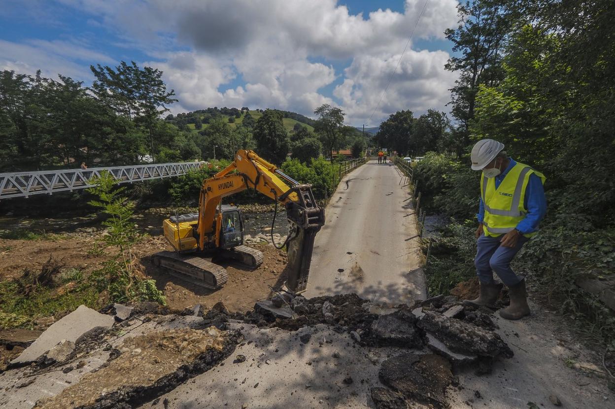 Una máquina trabaja en la demolición del puente y al fondo, la pasarela habilitada para los peatones. 